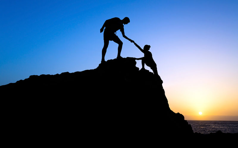 Man and woman help silhouette in mountains 5 Steps to Prioritize Your Success